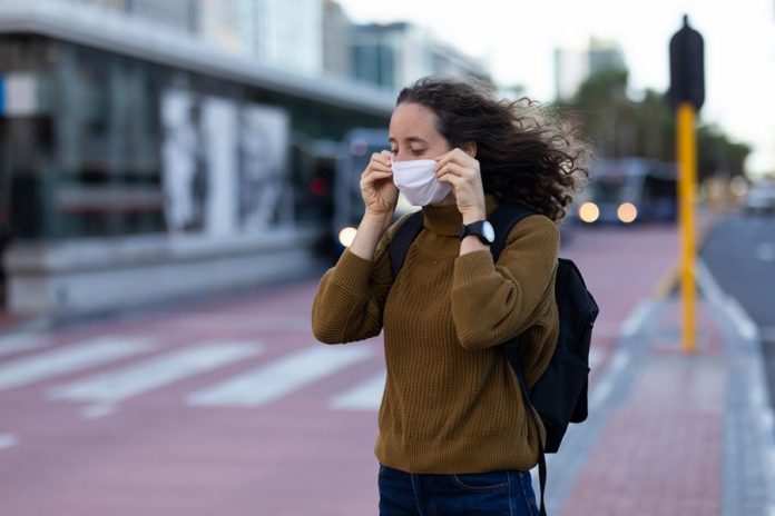 Caucasian woman out and about in the city streets during the day, putting on a face mask against covid19 coronavirus