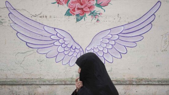 Iranian woman is walking past a mural in downtown Tehran