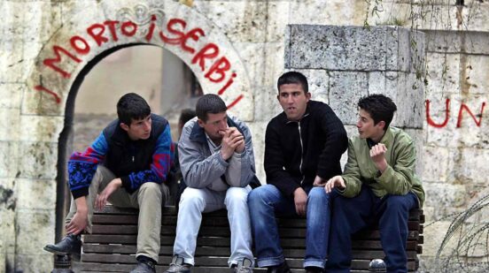Albanian youths chat in front of a destroyed church in Prizren